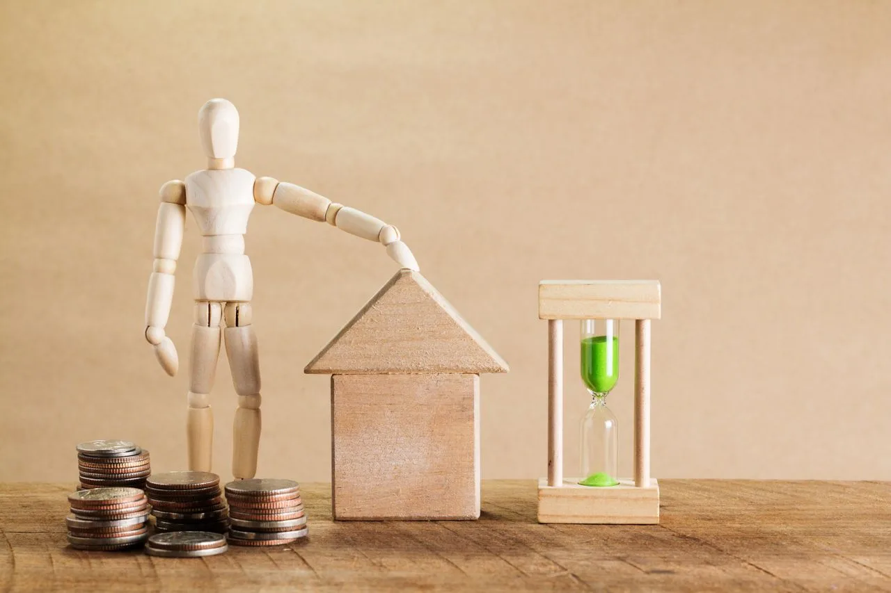 Houten figuur met een huisje, een zandloper en stapels muntstukken: timeshare koppelt je aan één vaste week per jaar en terugkerende kosten.